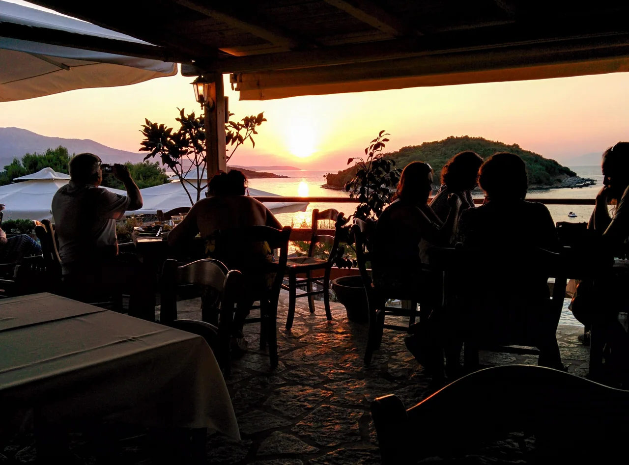 Diners sharing an evening at a seaside restaurant in Ksamil as the sun sets over the water