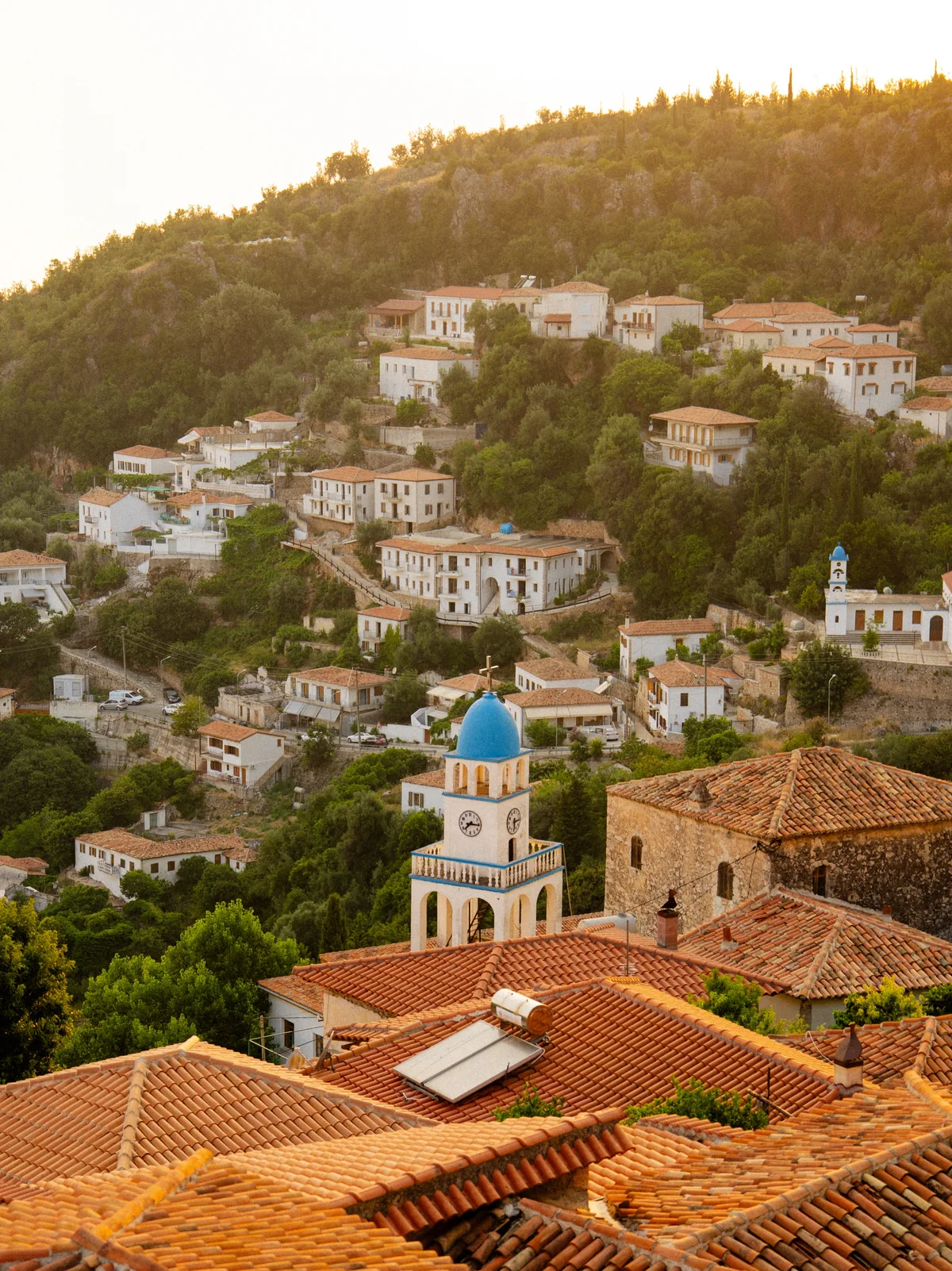Mediterranean hillside village with terracotta rooftops and blue-domed bell towers in golden sunlight